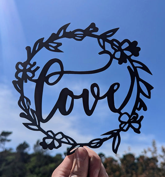 Offrez une décoration murale LOVE en métal entourée d'une couronne fleurie. Artisanat français, pièce romantique et moderne, expédiée depuis notre atelier.